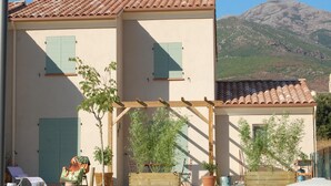 Un edificio de dos plantas con tejado de tejas, un balcón con barandilla de madera y un paisaje de montaña de fondo.