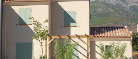 A two-story building with a tiled roof, a balcony with wooden railings, and a mountain backdrop.