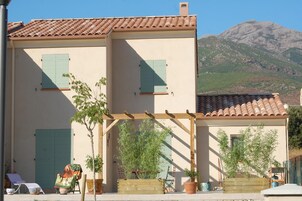 Un edificio de dos plantas con tejado de tejas, un balcón con barandilla de madera y un paisaje de montaña de fondo.