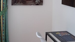 Una habitación con un cuadro grande de Buda, una silla blanca, una mesita pequeña y un equipo de aire acondicionado.