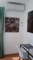 Una habitación con un cuadro grande de Buda, una silla blanca, una mesita pequeña y un equipo de aire acondicionado.