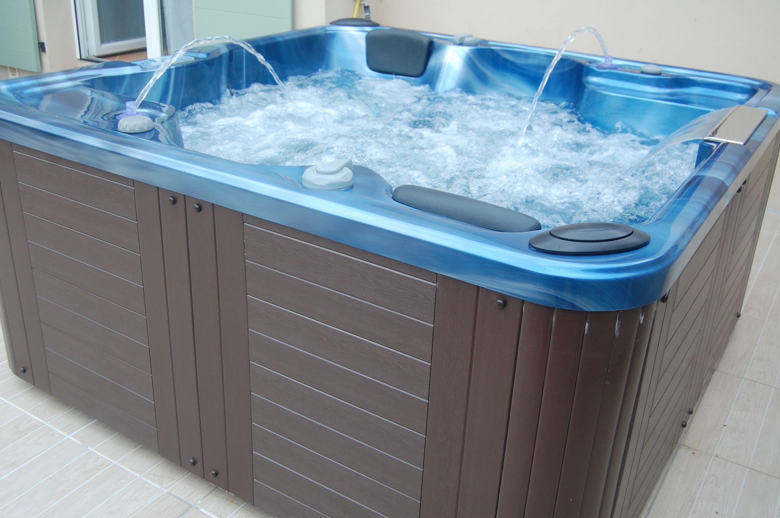 A hot tub with a blue exterior and a wooden interior, equipped with a control panel and a water pump.