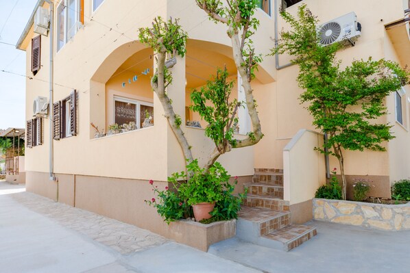 A building with a beige facade, a stone staircase, and a potted plant in front.