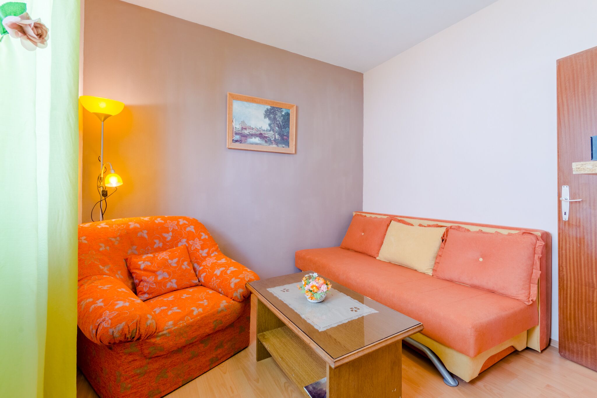 Een kleine kamer met een bank, een tafel en een lamp.