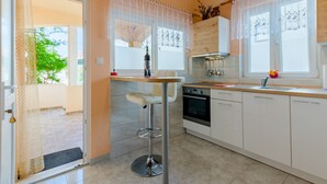 Een moderne keuken met witte kasten, een roestvrijstalen spoelbak en een dubbele oven. Er staat een barkruk en is een raam met kantgordijnen.