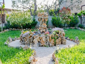Ein Garten mit einer zentralen Felsformation, umgeben von bunten Blumen und viel Grün.