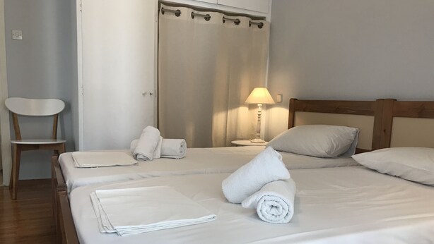 A neatly made bed with rolled towels, a wooden headboard, a nightstand with a lamp, and a chair. - Margaritas house (Athens)