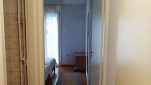 A hallway leading to a bedroom with a bed, a nightstand, and a window with curtains. - Margaritas house (Athens)