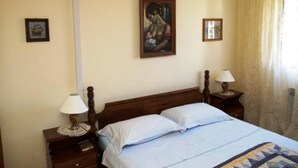 Een slaapkamer met een houten bed, twee nachtkastjes met lampen, een wandairconditioner en een schilderij aan de muur.