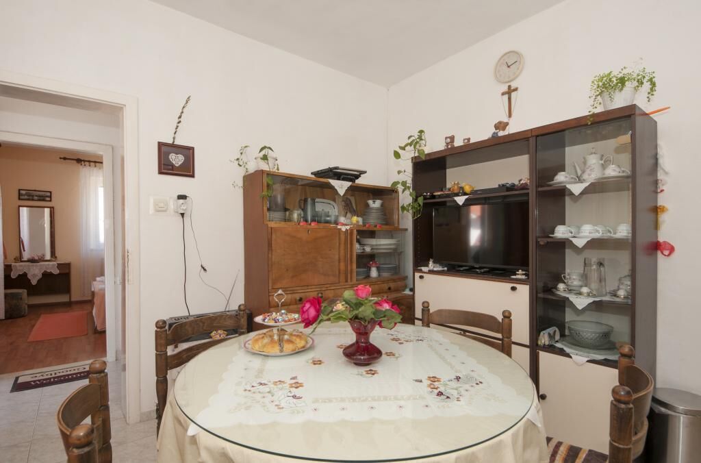 Un coin repas avec une table ronde recouverte d’une nappe en dentelle, entourée de chaises en bois. Un vase rempli de fleurs roses est posé sur la table.