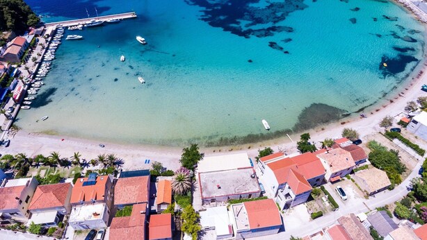 An aerial view of a coastal town with a marina, clear turquoise waters, and buildings with red-tiled roofs. - Apartments Dalmatin Žuljana - Studio Apartment 2 (Zuljana)