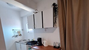A compact kitchenette with a stove, sink, and coffee maker. There is a small dining area with a chair and a table. - Apartments Dalmatin Žuljana - Studio Apartment 2 (Zuljana)