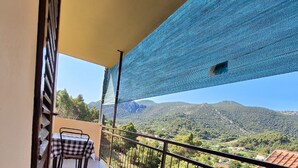 A balcony with a checkered table and chairs, a view of a mountainous landscape, and a blue mesh awning. - Apartments Dalmatin Žuljana - Studio Apartment 2 (Zuljana)