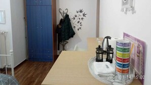 A room with a wooden table, a blue wardrobe, a coat rack with a jacket, a wall art of leaves, and a tray with coffee cans. - Modern ideally located studio apartment (Athens)