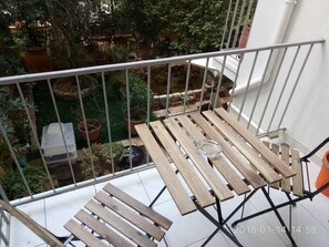 A balcony with a wooden table and chairs, a small garden area with potted plants, and a white railing. - Modern ideally located studio apartment (Athens)