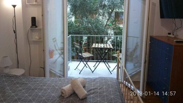A bedroom with a bed, a bedside table, a lamp, a TV, a wardrobe, and a balcony with a table and chairs. - Modern ideally located studio apartment (Athens)