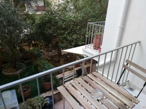 A balcony with a wooden bench, potted plants, and a view of a garden. - Modern ideally located studio apartment (Athens)