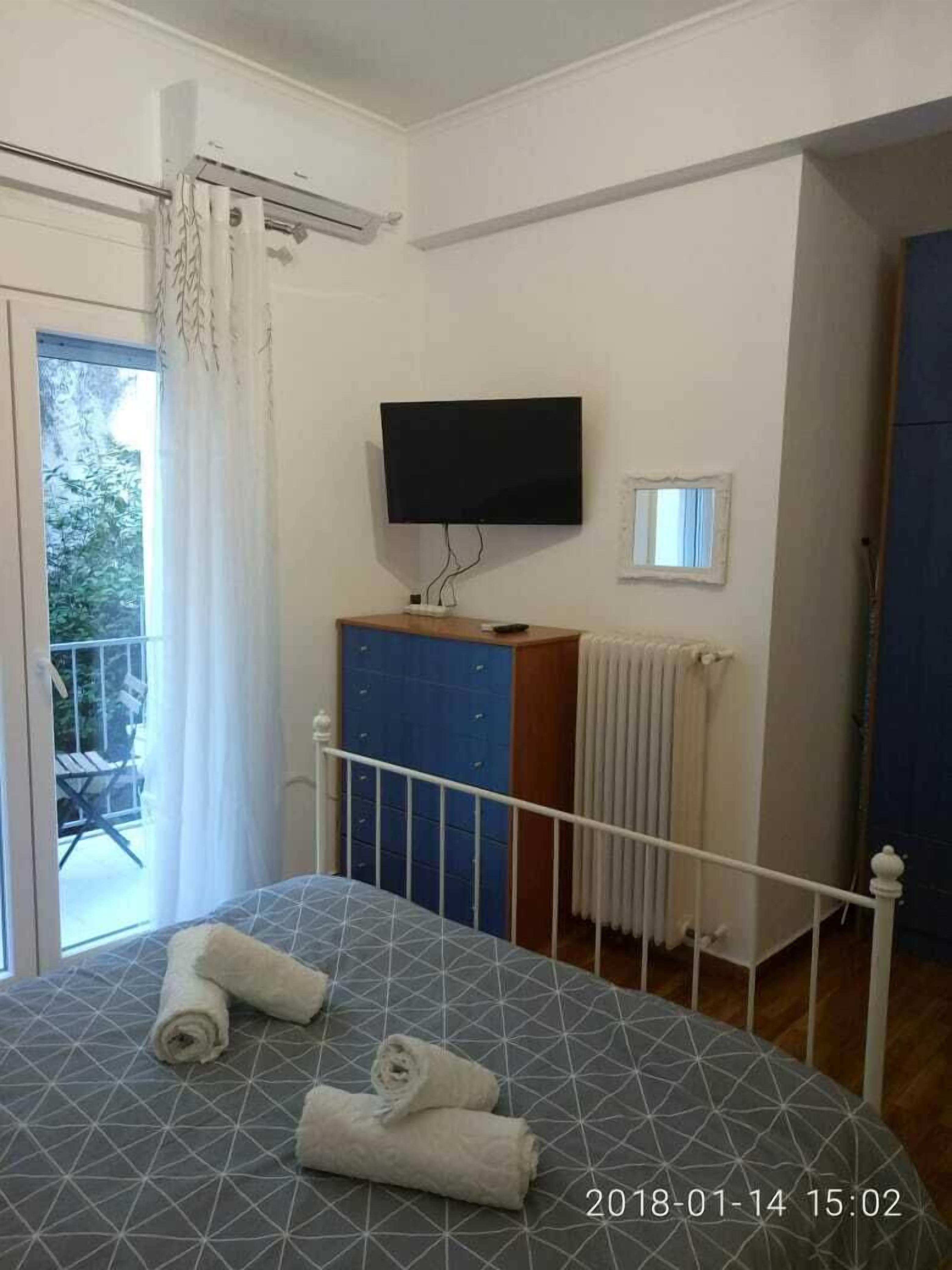 A bedroom with a bed, a TV mounted on the wall, a small window, and a radiator.