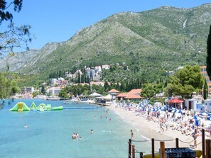 A beach with clear water, a sandy shore, and a mountainous backdrop.