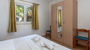 Un dormitorio con cama, armario, silla y ventana con cortinas.