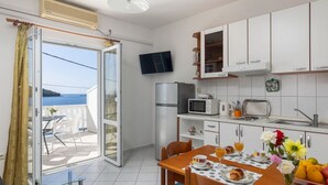 Cocina compacta con comedor, televisor montado en la pared y vista al mar a través de un ventanal corredero.