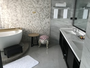 Un baño moderno con una bañera independiente, un taburete pequeño, un tocador con espejo y suelo de baldosas.