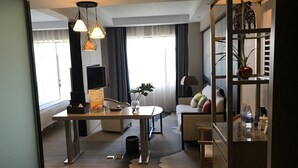 A modern hotel room with a dining area, a sofa, a coffee table, and a TV. - Metropolis Golf Hot Spring Hotel (Kunming)