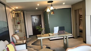 A modern hotel room with a large bed, a sitting area with a round table, and a desk with a computer and a phone. - Metropolis Golf Hot Spring Hotel (Kunming)