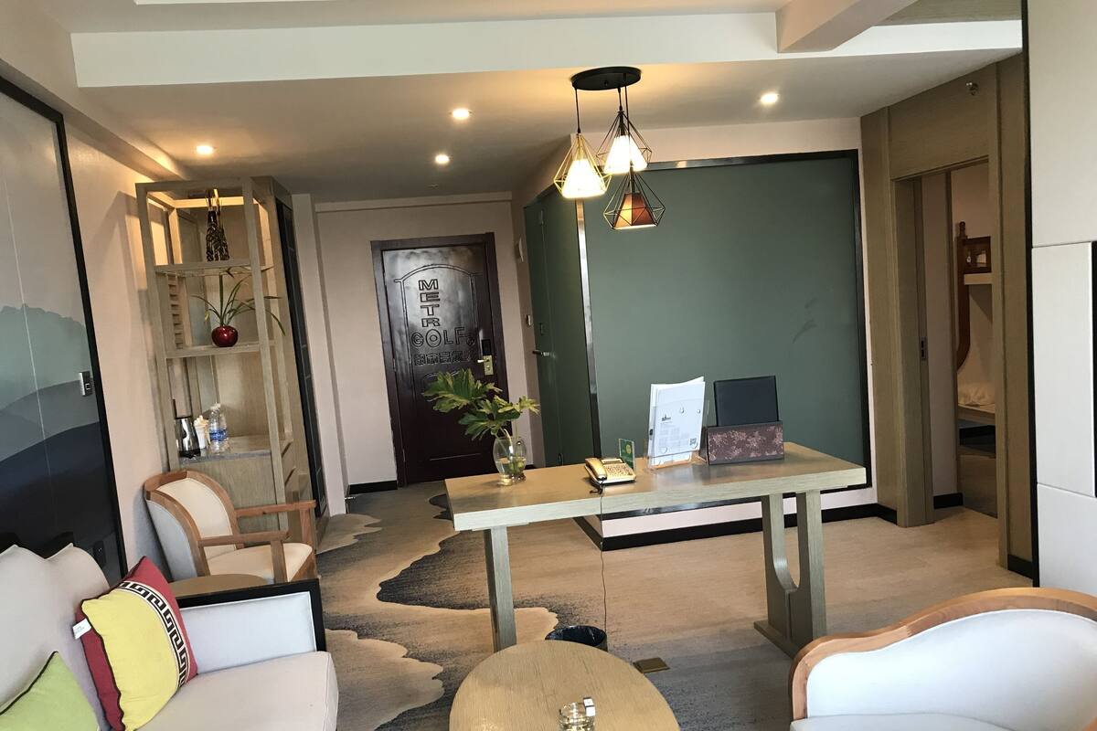 Une chambre d’hôtel moderne dotée d’un grand lit, d’un coin salon avec une table ronde et d’un bureau avec un ordinateur et un téléphone.