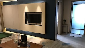 A modern living room with a flat-screen TV mounted on a wall, a wooden coffee table with bottled water, and a small side table with a plant. - Metropolis Golf Hot Spring Hotel (Kunming)