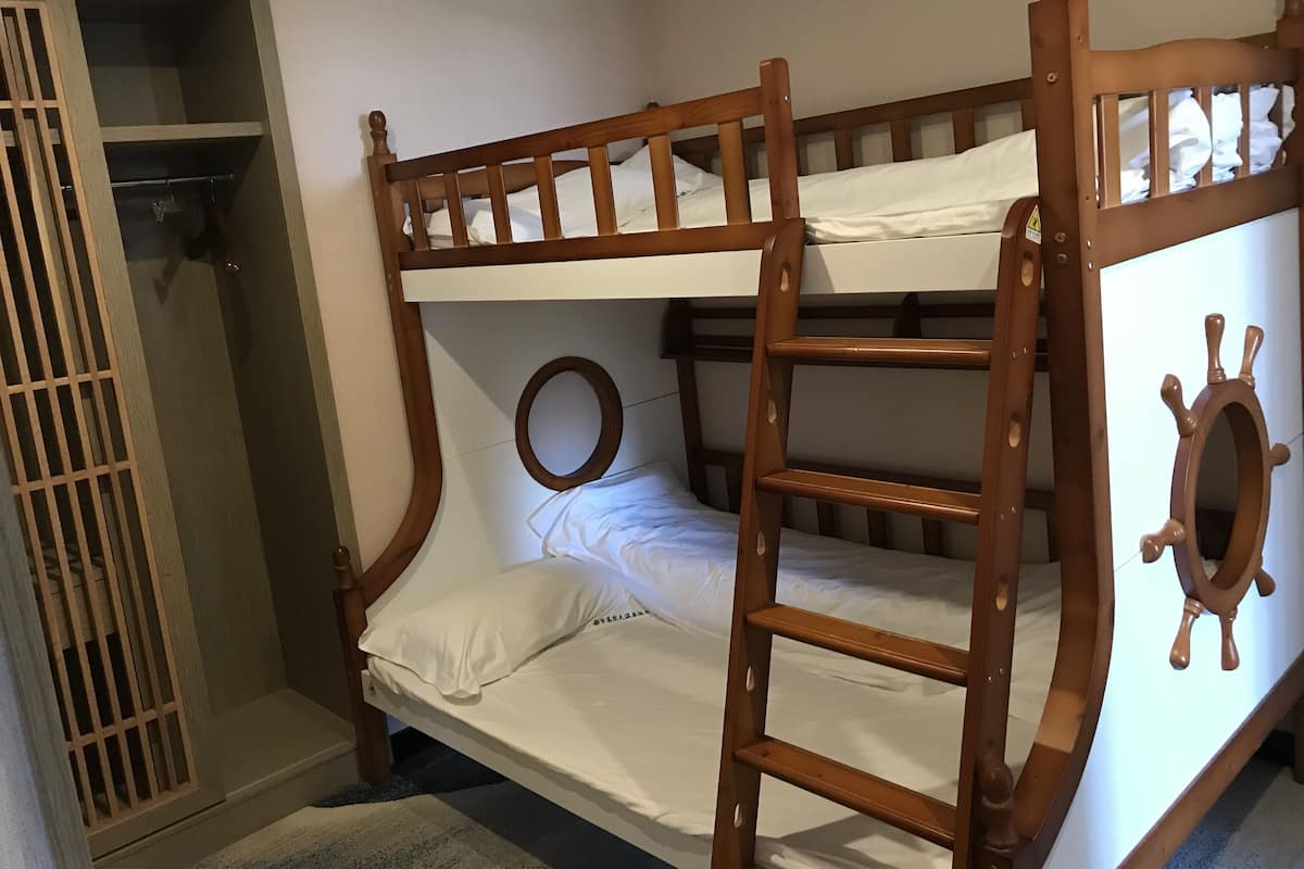Un lit superposé avec une échelle, un miroir rond et une armoire à motifs géométriques.