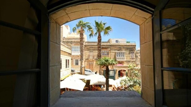 An arched doorway leading to a courtyard with palm trees and a building in the background. - Cittadella Boutique Living (Victoria)