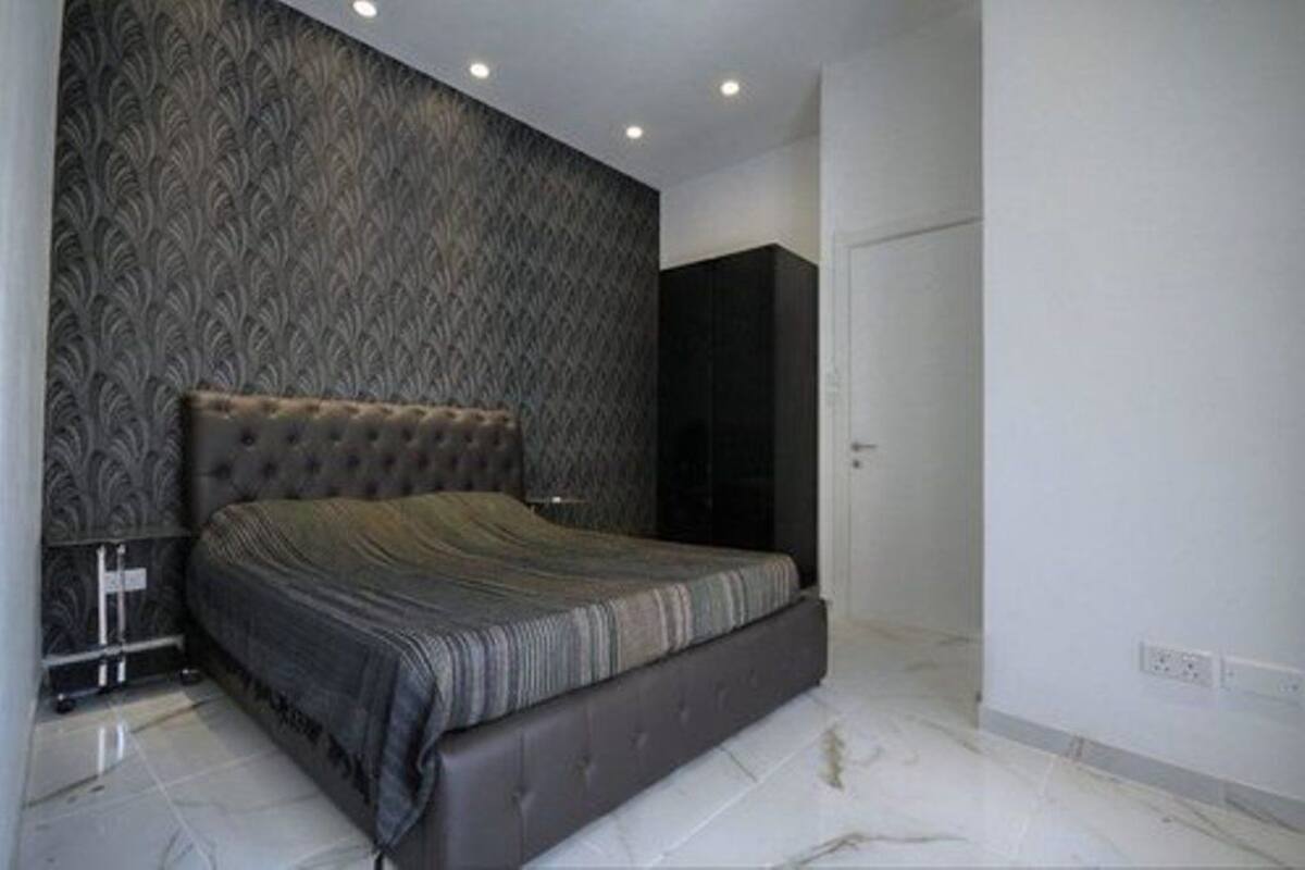 A modern bedroom with a tufted headboard, a large bed, and a patterned wallpaper.
