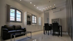 A modern living room with a black leather sofa, a glass coffee table, and a dining area with a chandelier. - Cittadella Boutique Living (Victoria)