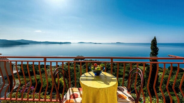 Un balcon avec une table et des chaises, donnant sur un lac paisible où l’on aperçoit des îles au loin.