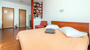 Une chambre d’hôtel avec un lit, une chaise rouge, une bibliothèque en bois et deux portes.