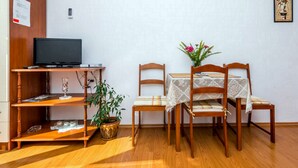 Une petite pièce avec un meuble en bois pour la télévision, une table avec deux chaises, une plante en pot et un tableau encadré au mur.