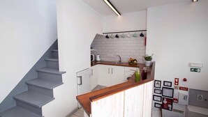 A modern kitchen with white cabinets, a wooden countertop, and a staircase. - GiG Capsule Hostel (Mafra)
