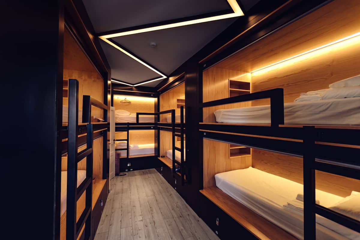 A narrow, dimly lit corridor with bunk beds on either side, wooden walls, and a wooden floor.
