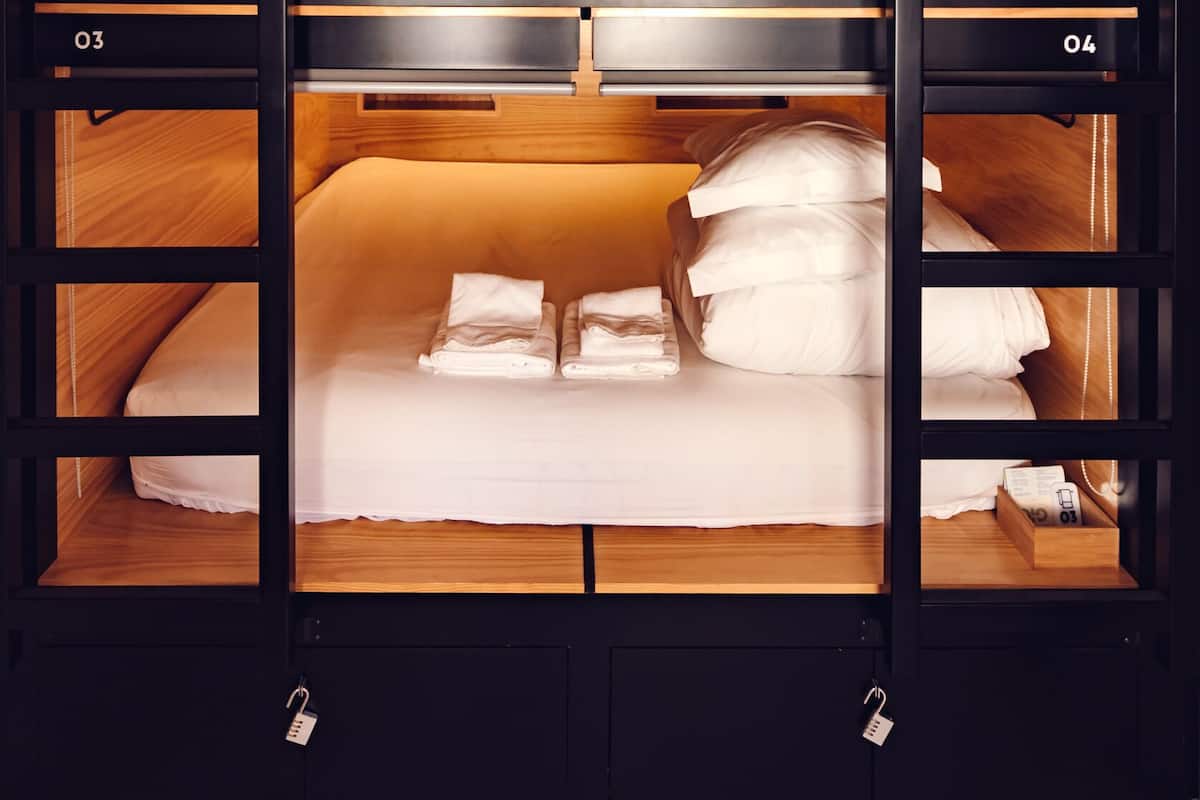 A bunk bed with two levels, each with a wooden frame and a white mattress. There are storage compartments below each bed, and the room has a warm, wooden interior.