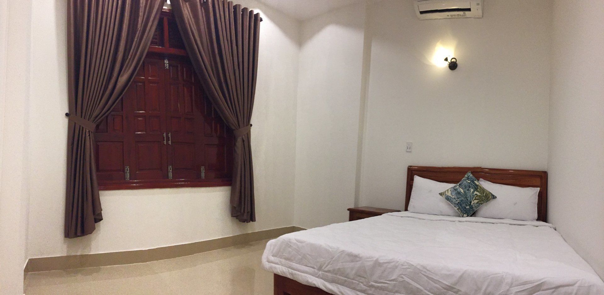 Un dormitorio con cama, mesita de noche, aire acondicionado instalado en la pared y ventana con cortinas.