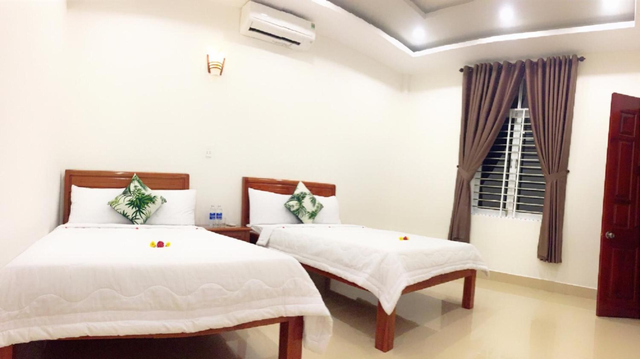 A hotel room with two beds, a ceiling fan, an air conditioning unit, a window with curtains, and a door.