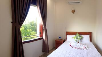 A hotel room with a bed, a nightstand, a window with curtains, and a view of greenery outside.
