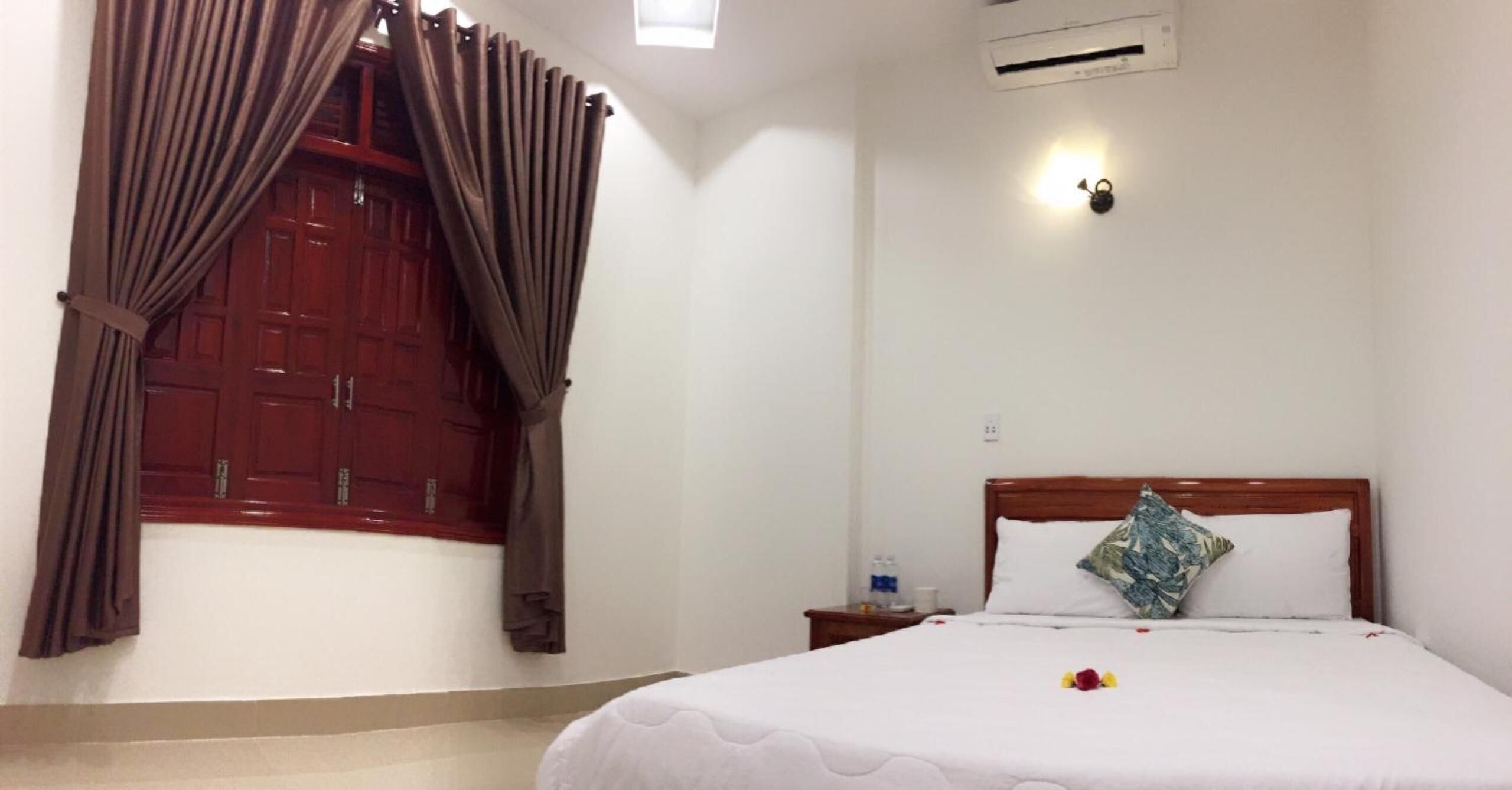 Habitación de hotel con cama, mesita de noche, ventana con cortinas y aire acondicionado.