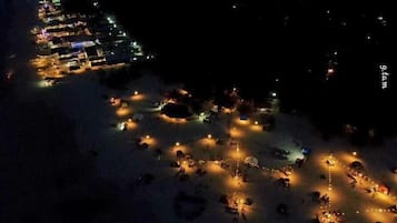 An aerial view of a resort with multiple buildings, a beach area with people and lights, and a large body of water.