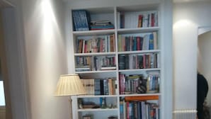 A narrow hallway with a white bookshelf filled with books, a small table with a lamp, and a radiator on the right. - Luxury Flat with Amazing Lycabetus View (Athens)