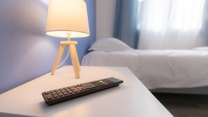 Un lit avec une literie blanche, une table de chevet avec une lampe et une télécommande.