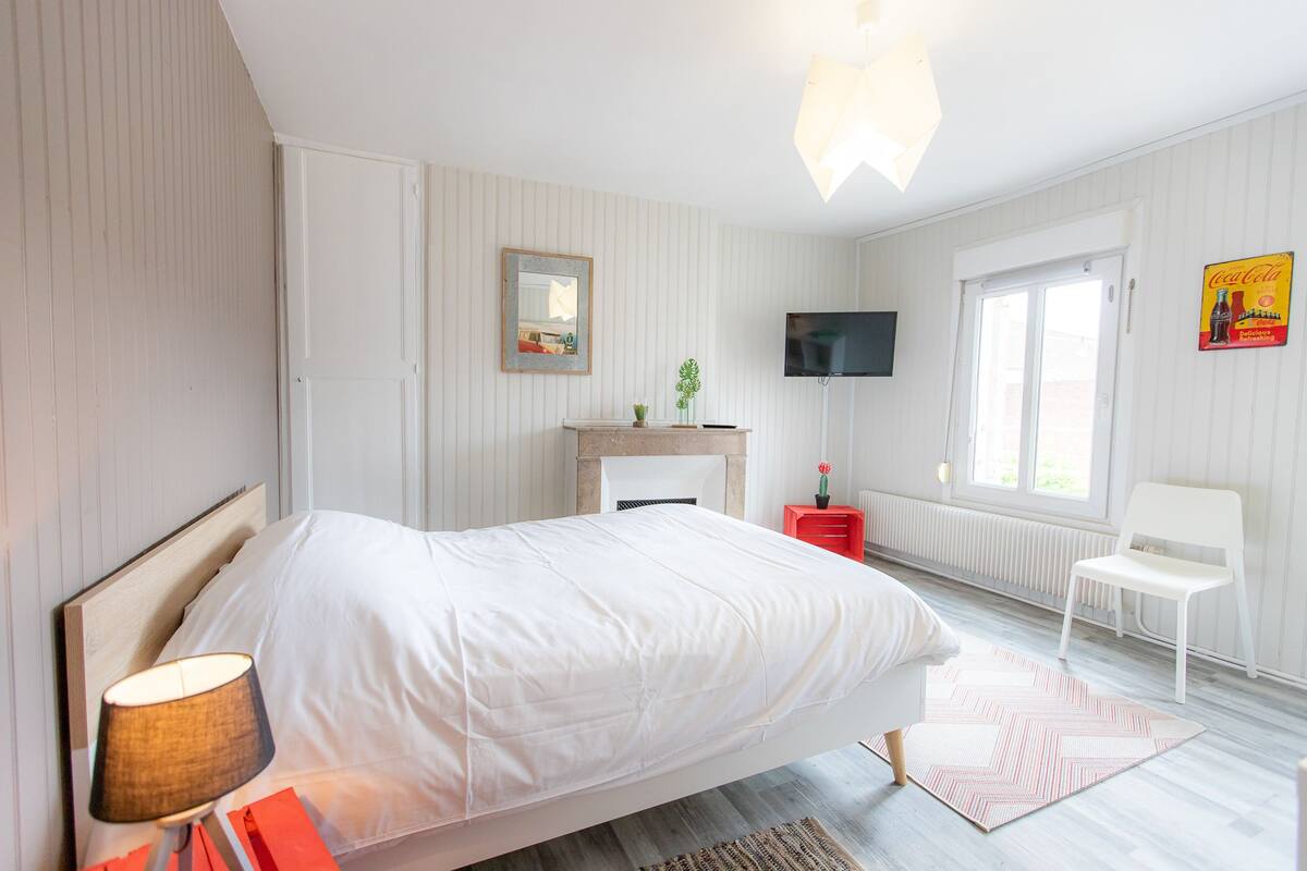A bedroom with a bed, a TV, a fireplace, and a window.