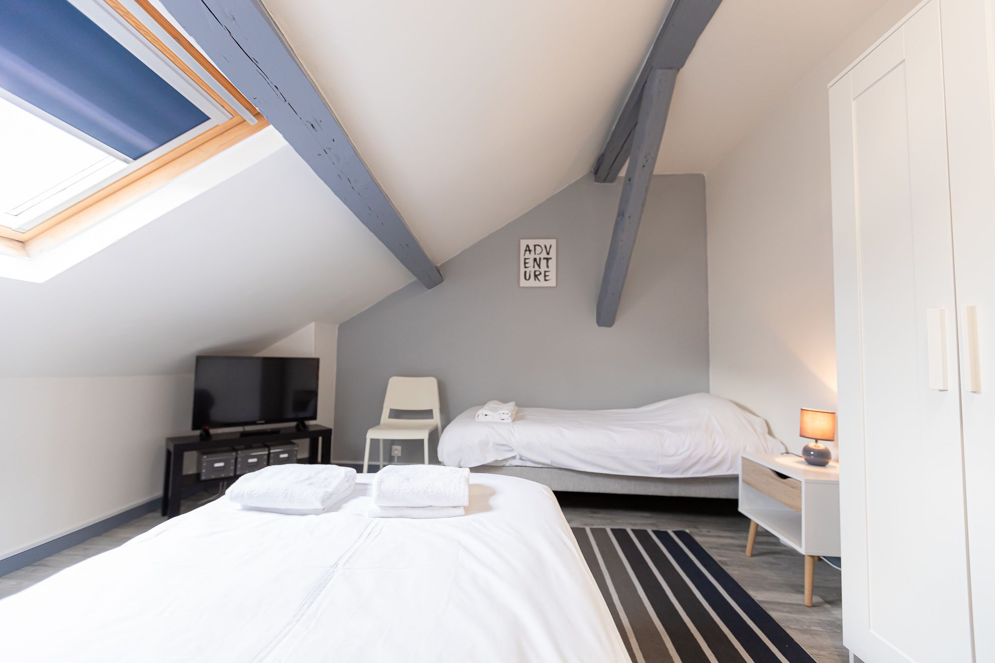 A bedroom with two beds, a TV, a desk with a lamp, and a sign that says "ADVENTURE".