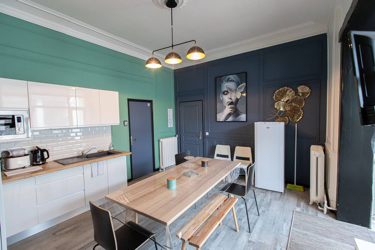 A modern kitchen with white cabinets, a wooden countertop, and a built-in microwave. There is a dining area with a wooden table and chairs, and a refrigerator.